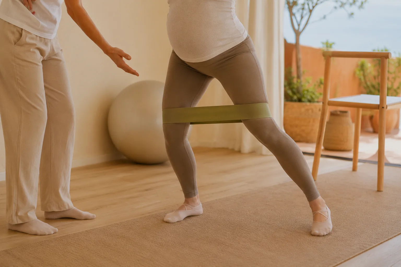 Mujer embarazada trabajando fuerza de piernas con una banda elástica, supervisada por su fisioterapeuta