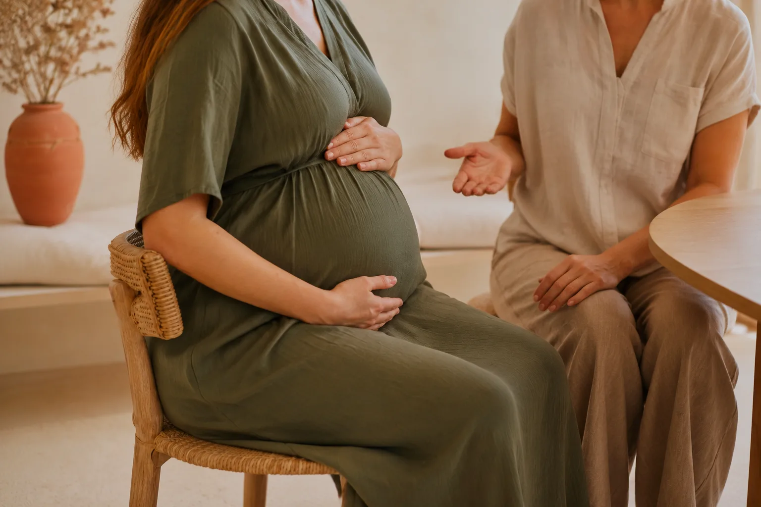 Mujer embarazada sentada sujetándose el abdomen mientras conversa con su fisioterapeuta